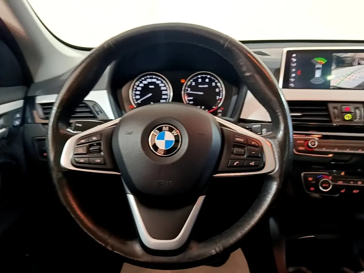 Vue intérieure centrée sur le volant cuir noir d’une BMW X1 2020 avec tableau de bord et écran tactile visible à droite.