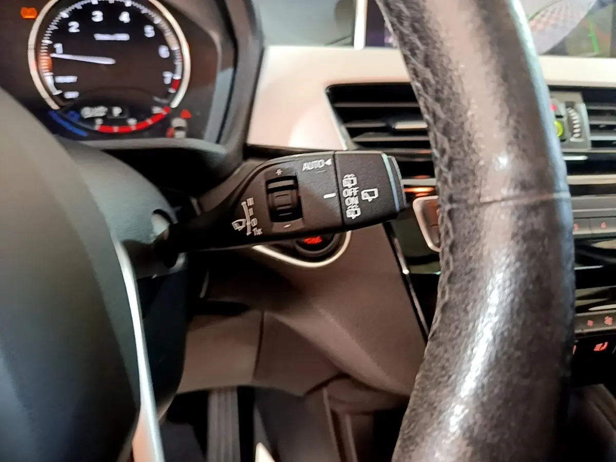 Vue intérieure rapprochée du volant cuir noir et du commodo d’essuie-glace d’une BMW X1 sDrive20i 2020.