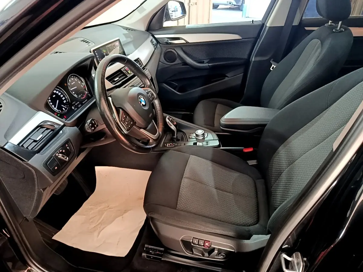 Vue intérieure côté conducteur d’un BMW X1 noir, montrant le volant cuir multifonctions et la console centrale avec écran tactile.