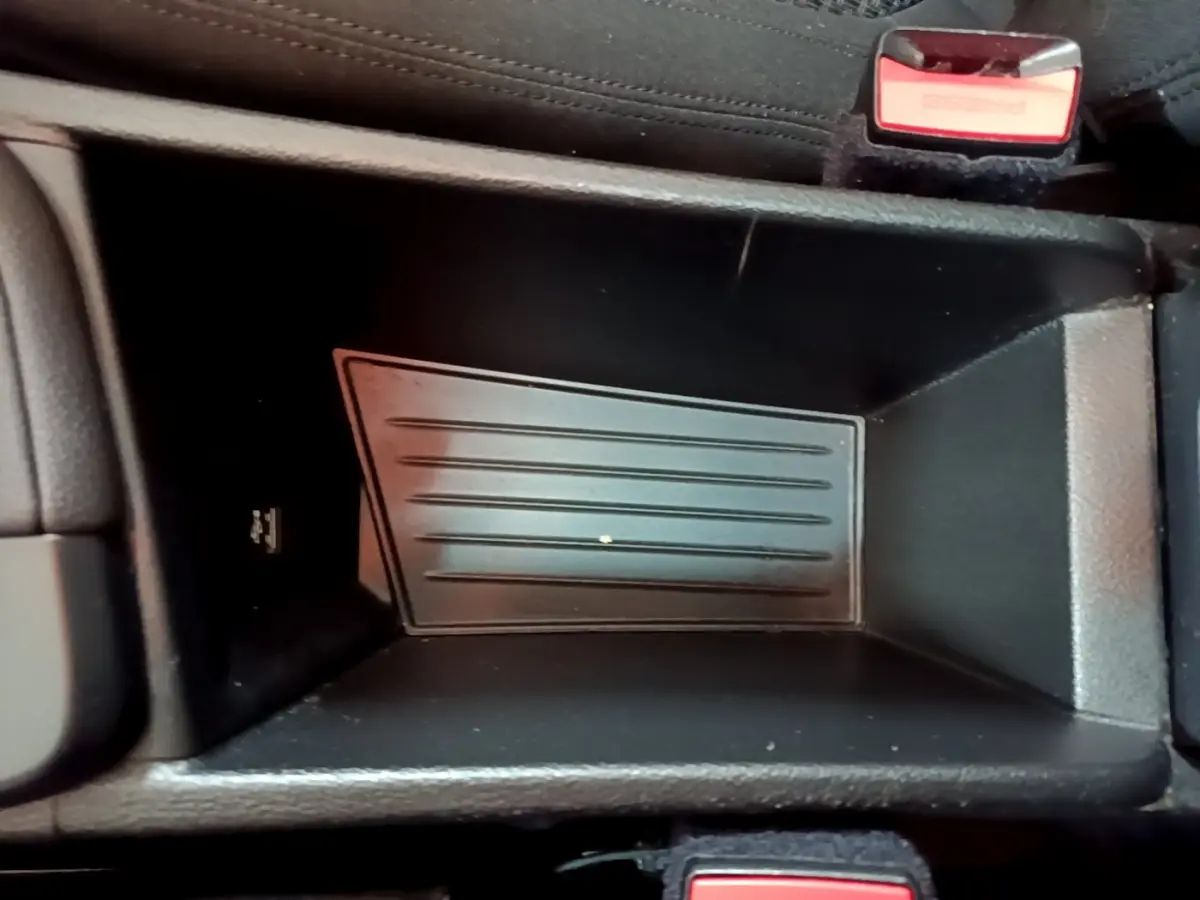 Gros plan sur le rangement central noir du BMW X1 sDrive20i, avec bouton de sécurité rouge visible en haut à droite.