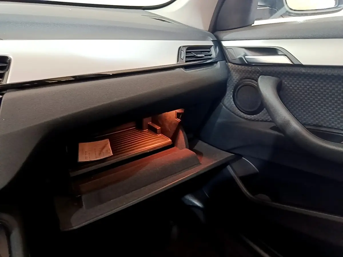 Intérieur BMW X1 2020, vue côté passager sur boîte à gants ouverte avec éclairage orange et garnitures noires et grises.