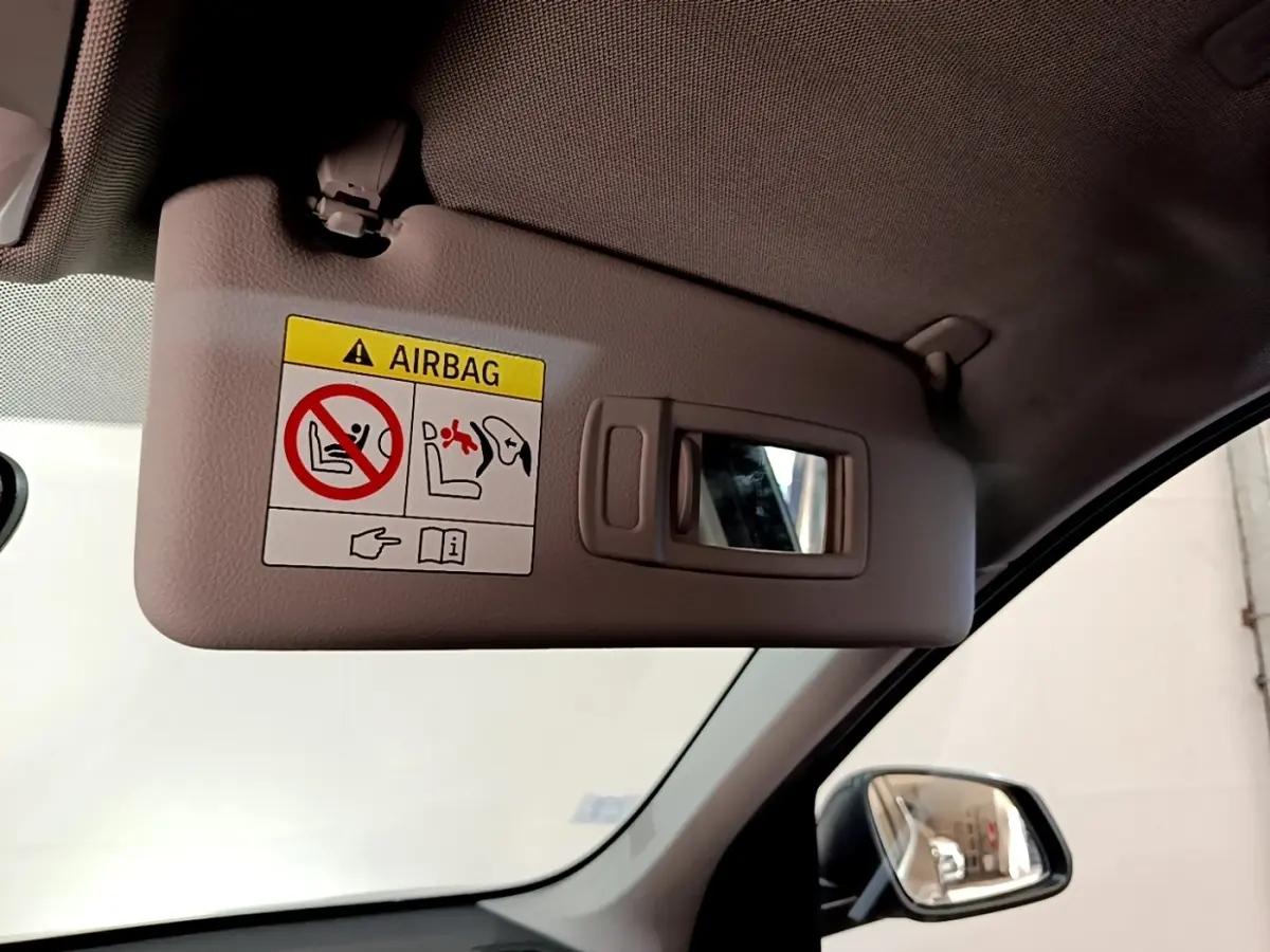 Détail intérieur du pare-soleil côté conducteur avec miroir et avertissement airbag dans une BMW X1 noire de 2020.
