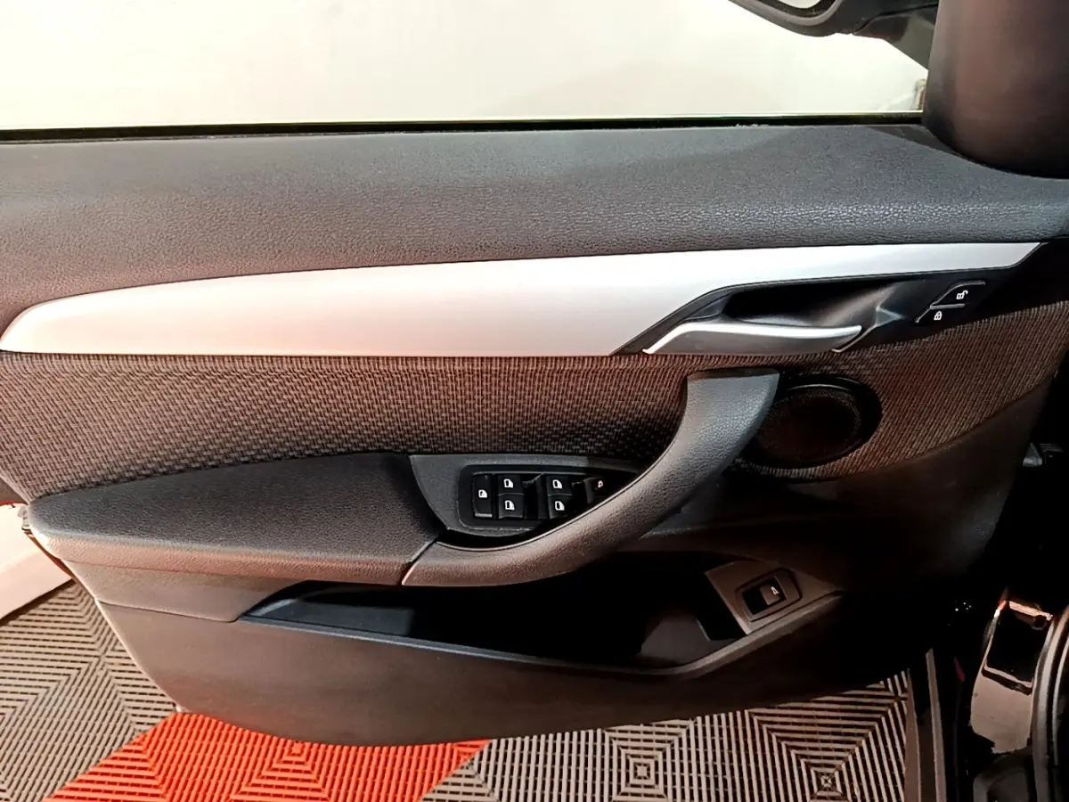 Vue intérieure côté gauche de la porte avant d'une BMW X1 noire, avec commandes de vitres et poignée intégrée.