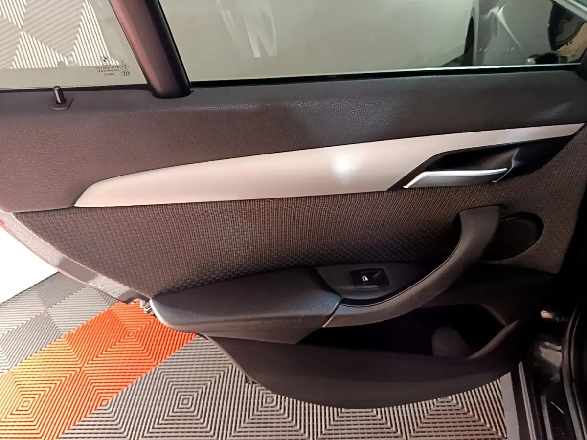 Vue rapprochée de la porte arrière gauche noire d’un BMW X1 2020 avec poignée et bouton de verrouillage intégré.