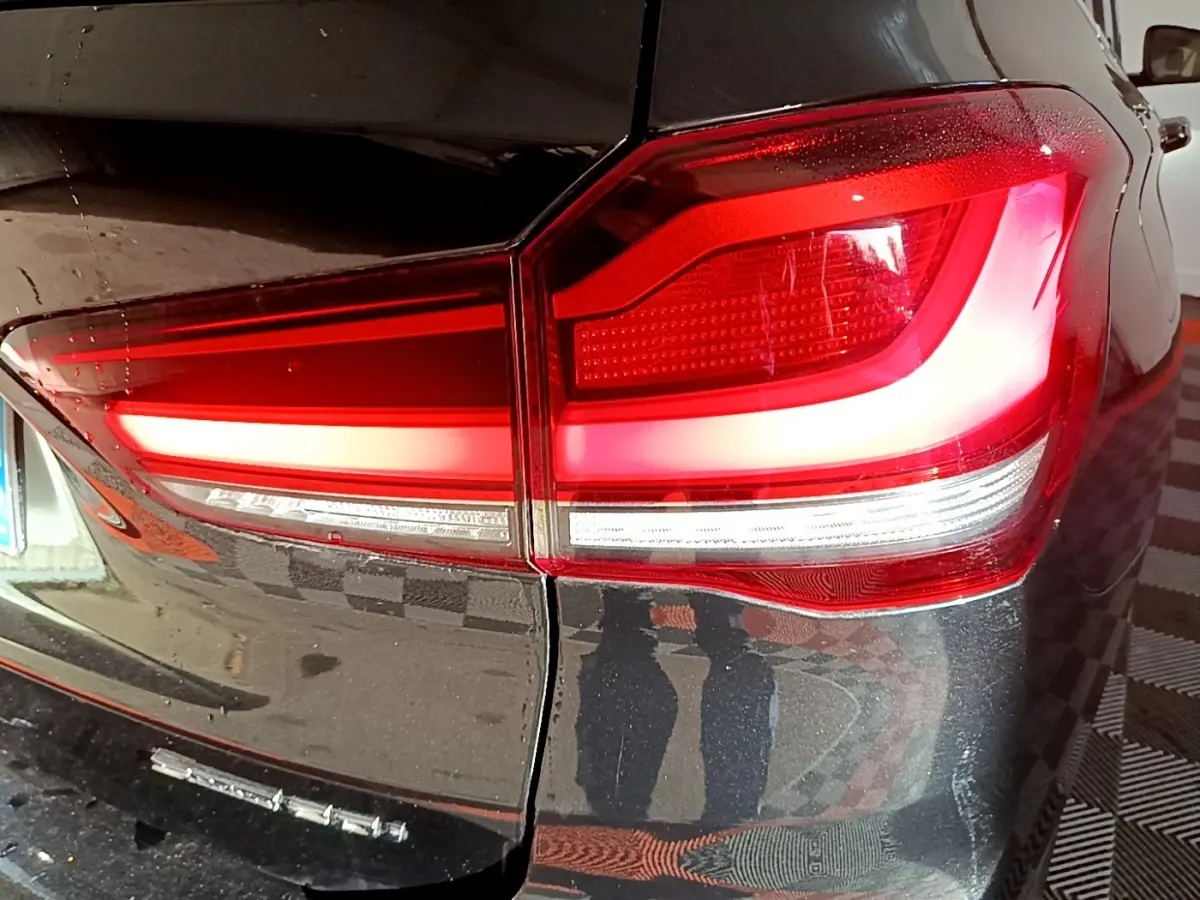 Gros plan sur le feu arrière droit rouge et blanc d’un BMW X1 noir, avec reflet sur la carrosserie brillante.