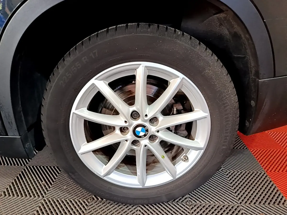 Gros plan sur la roue avant droite d’un BMW X1 noir, jante alliage argentée à 10 branches.