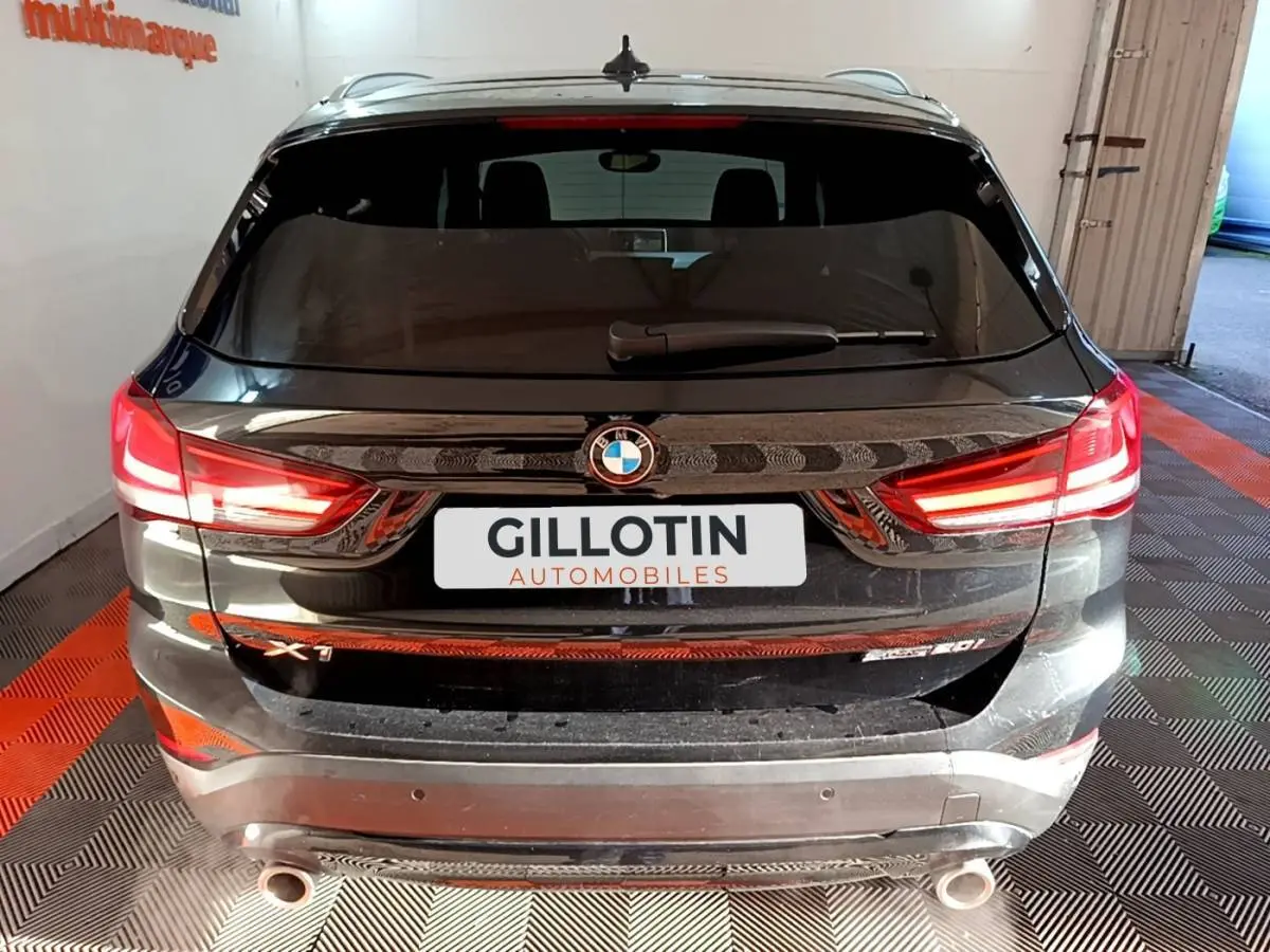 Vue arrière d’un BMW X1 sDrive20i noir avec feux LED allumés et double sortie d’échappement visible.