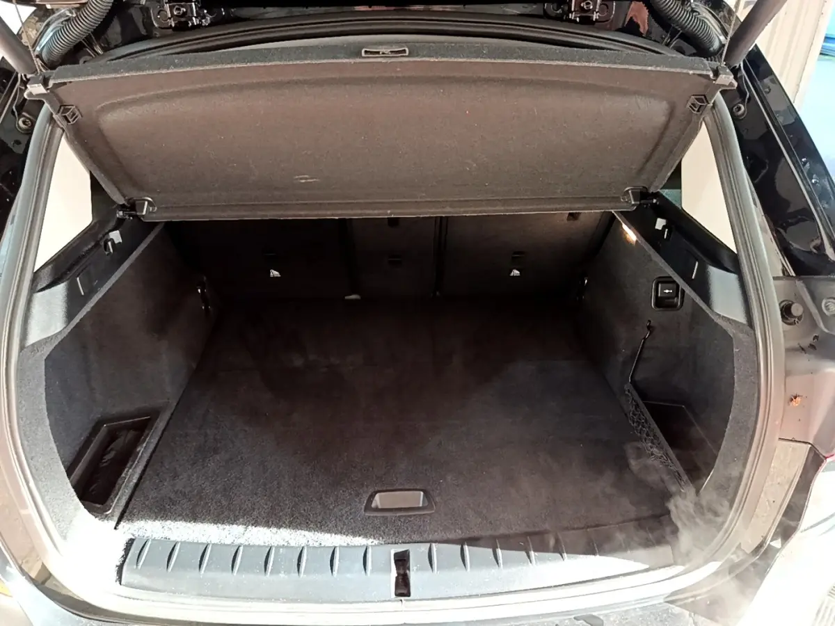 Coffre ouvert vu de l'arrière d'un BMW X1 noir, montrant un espace de rangement propre et bien agencé.