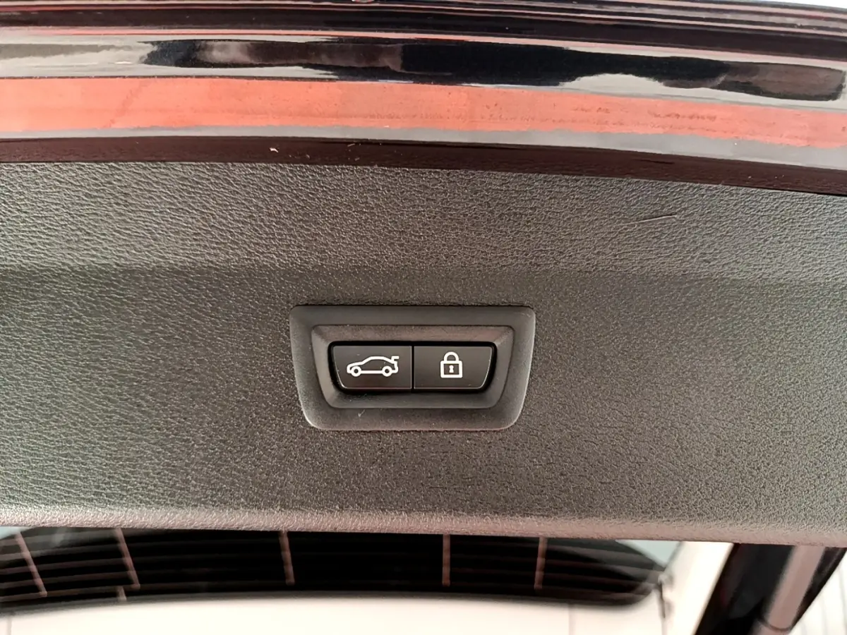 Boutons de fermeture et verrouillage électrique du coffre sur le hayon d’un BMW X1 noir, vue intérieure rapprochée.
