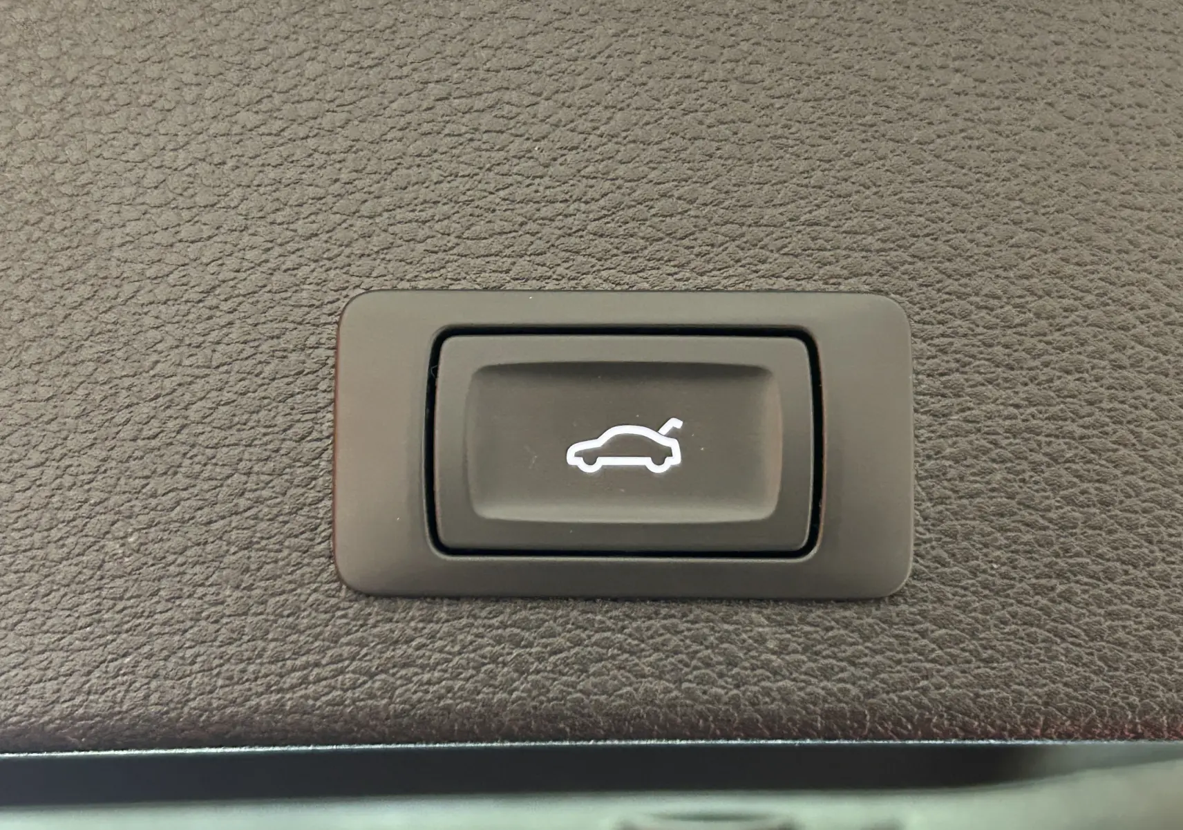 Bouton noir de hayon électrique avec icône blanche sur panneau en cuir marron dans un Audi Q2 gris 2023.