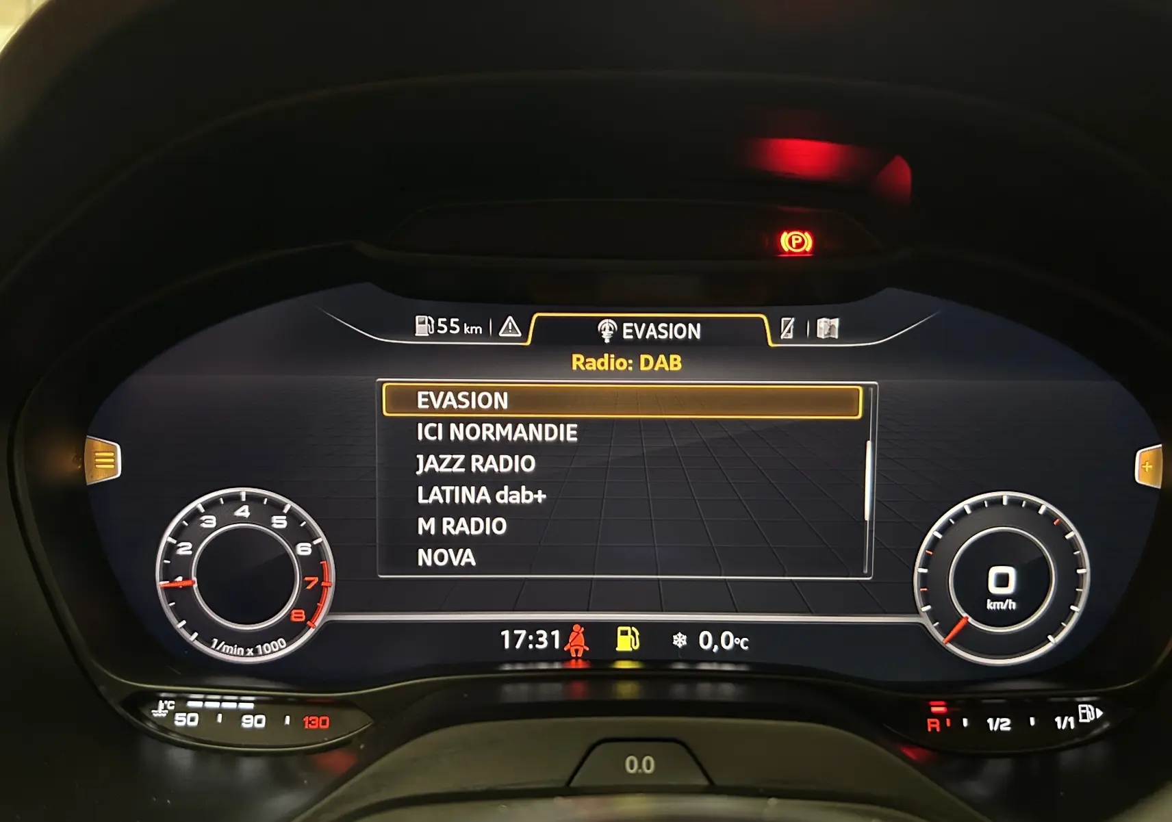 Affichage du virtual cockpit de l'Audi Q2 gris 2023, montrant la liste des radios DAB et les compteurs numériques.