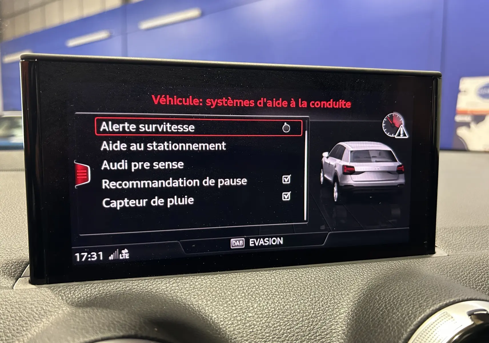 Écran central de l'Audi Q2 gris montrant les options d'aide à la conduite avec vue arrière du véhicule en 3/4.
