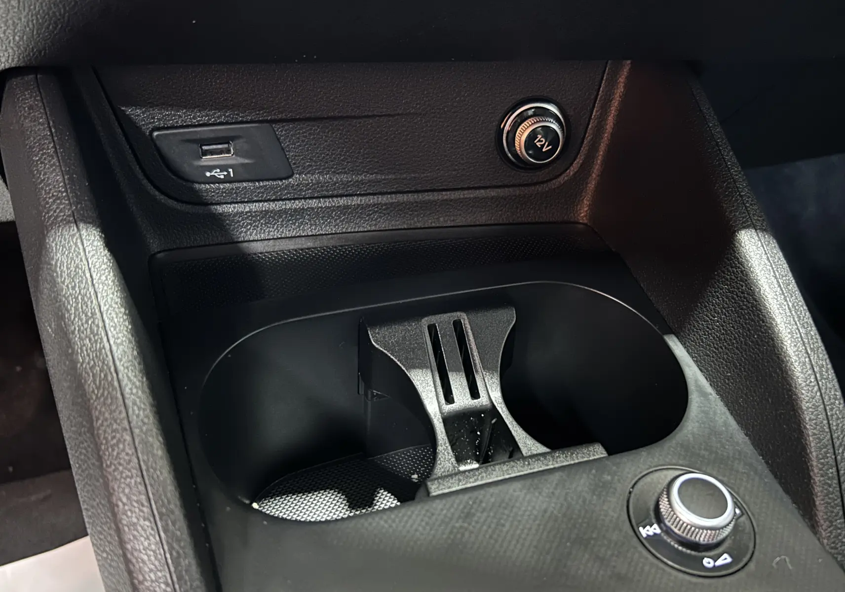Gros plan intérieur sur la console centrale noire de l'Audi Q2 avec prise USB, prise 12V et porte-gobelets.