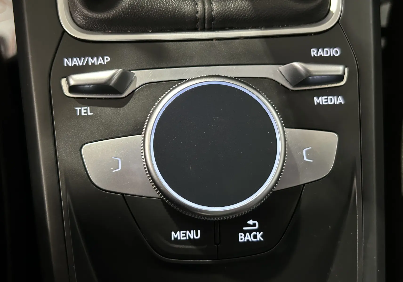 Gros plan sur la molette de commande centrale noire et argentée de l'Audi Q2 gris, avec boutons NAV/MAP, RADIO et MENU visibles.