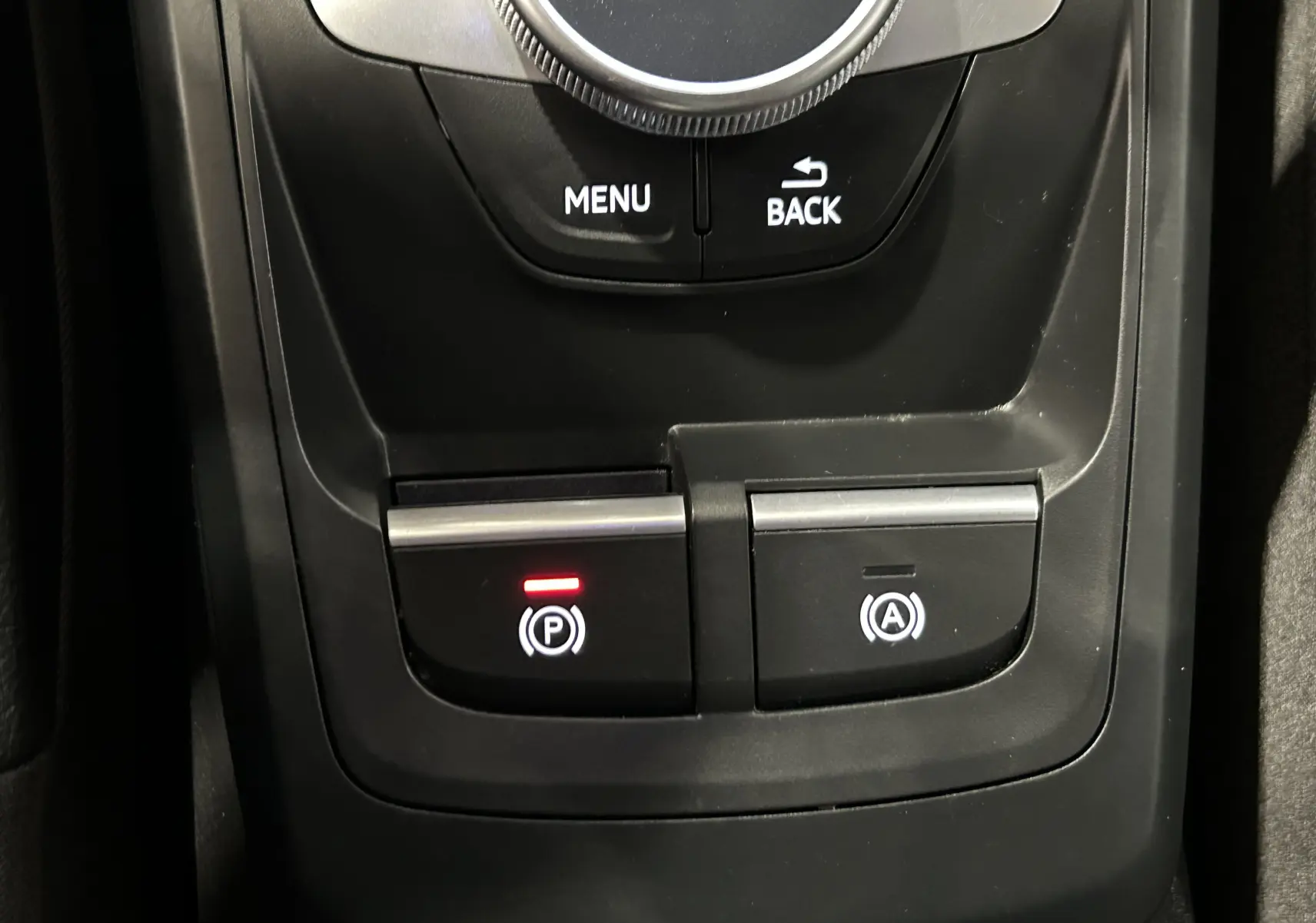 Gros plan sur la console centrale noire de l'Audi Q2 avec boutons de frein à main électronique et arrêt auto.