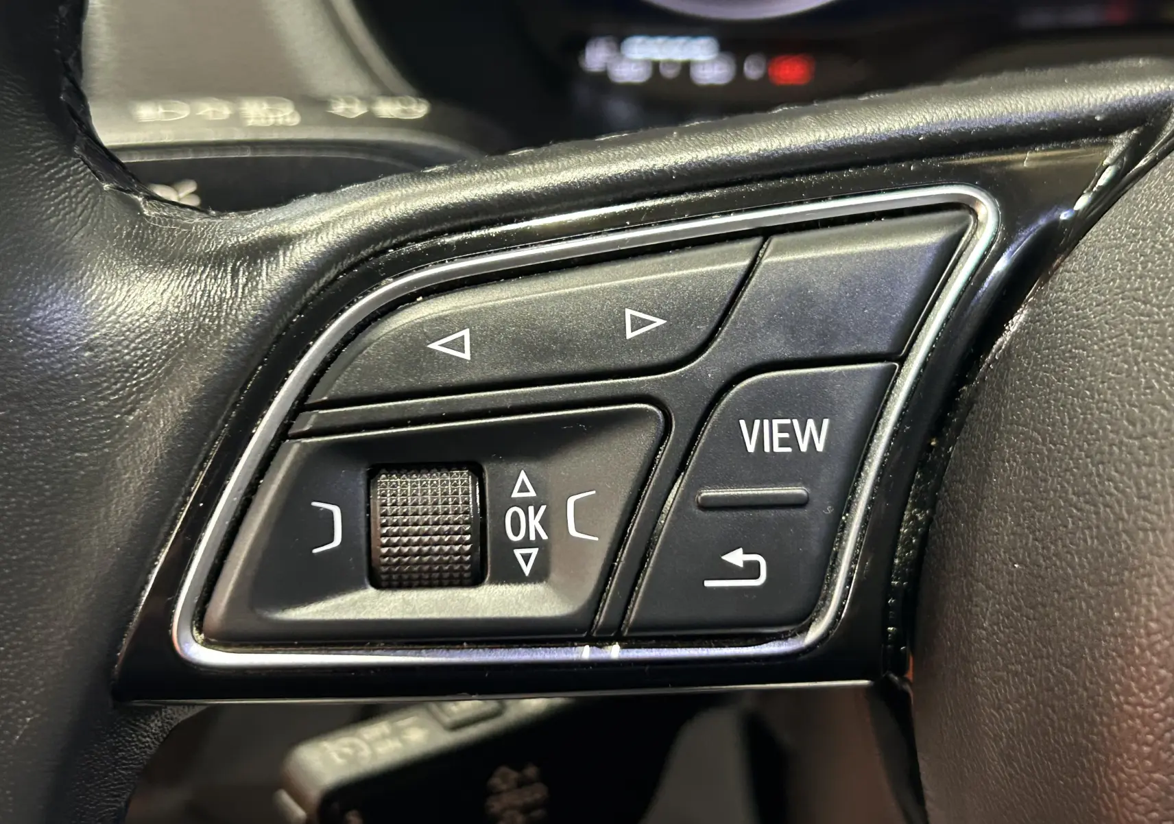 Gros plan sur les commandes noires du volant en cuir de l'Audi Q2 gris, avec boutons de navigation et fonction View.