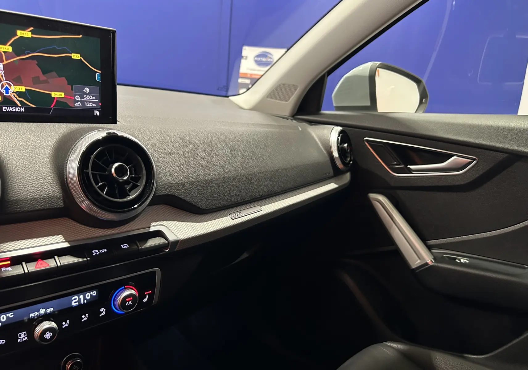 Intérieur côté passager de l'Audi Q2 gris 2023, avec tableau de bord moderne et écran GPS en vue rapprochée.
