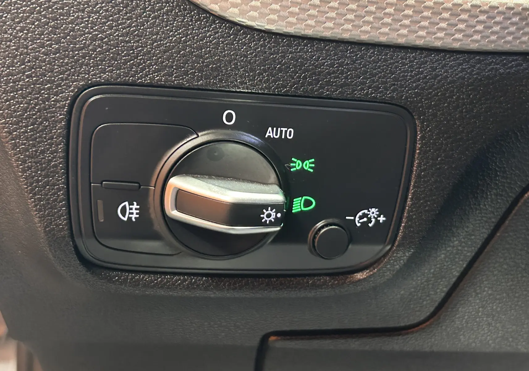 Gros plan sur le bouton de commande des phares avec indicateurs verts, sur le tableau de bord noir de l'Audi Q2 2023.