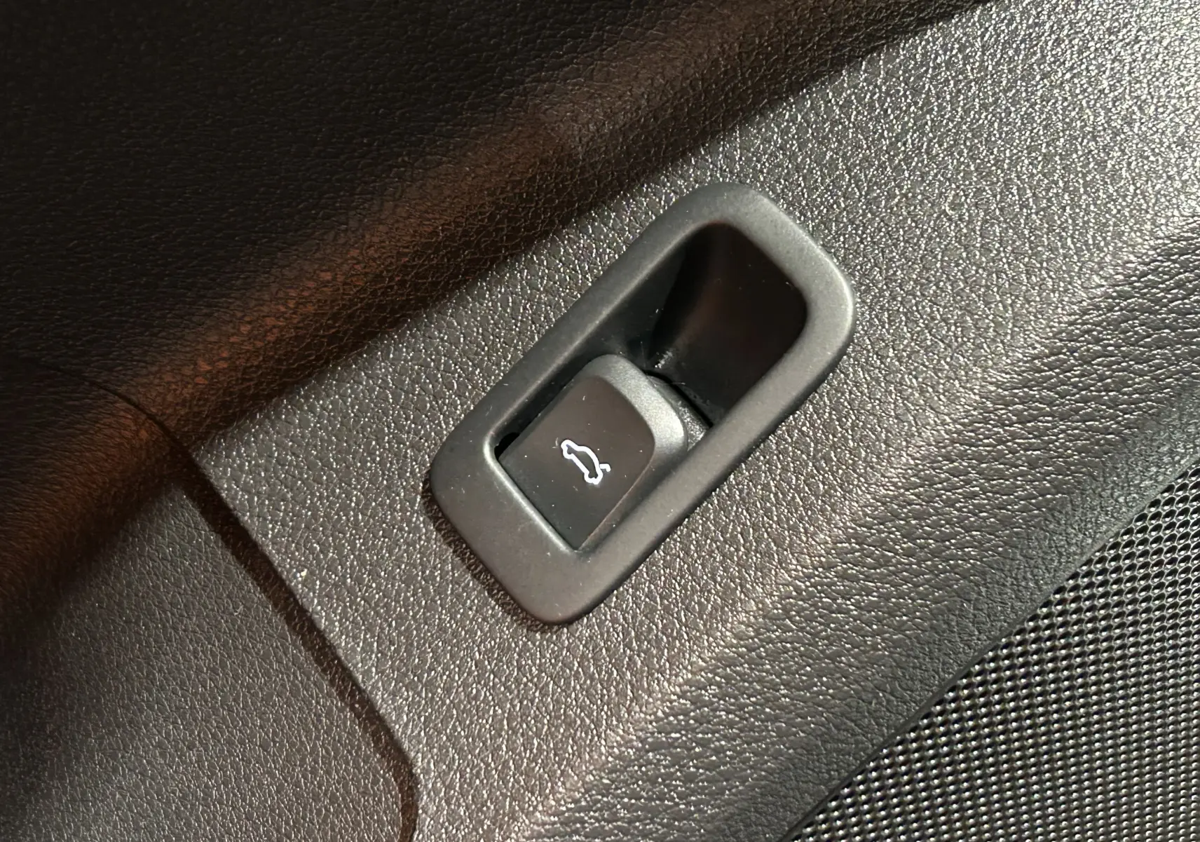 Bouton d'ouverture du hayon électrique sur la garniture intérieure noire d'un Audi Q2 gris, vue en gros plan.