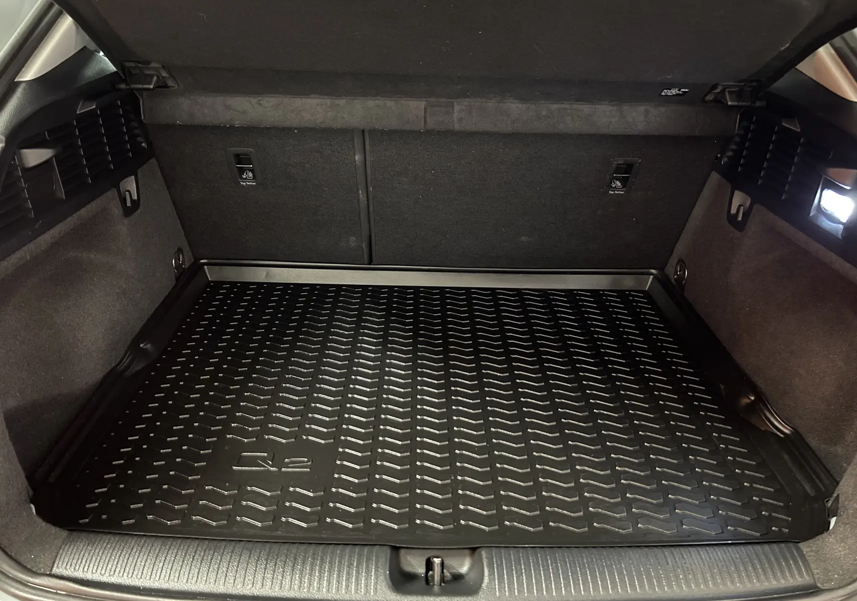 Coffre ouvert de l'Audi Q2 gris, vue intérieure montrant le tapis de coffre noir avec logo Q2 et éclairage latéral.