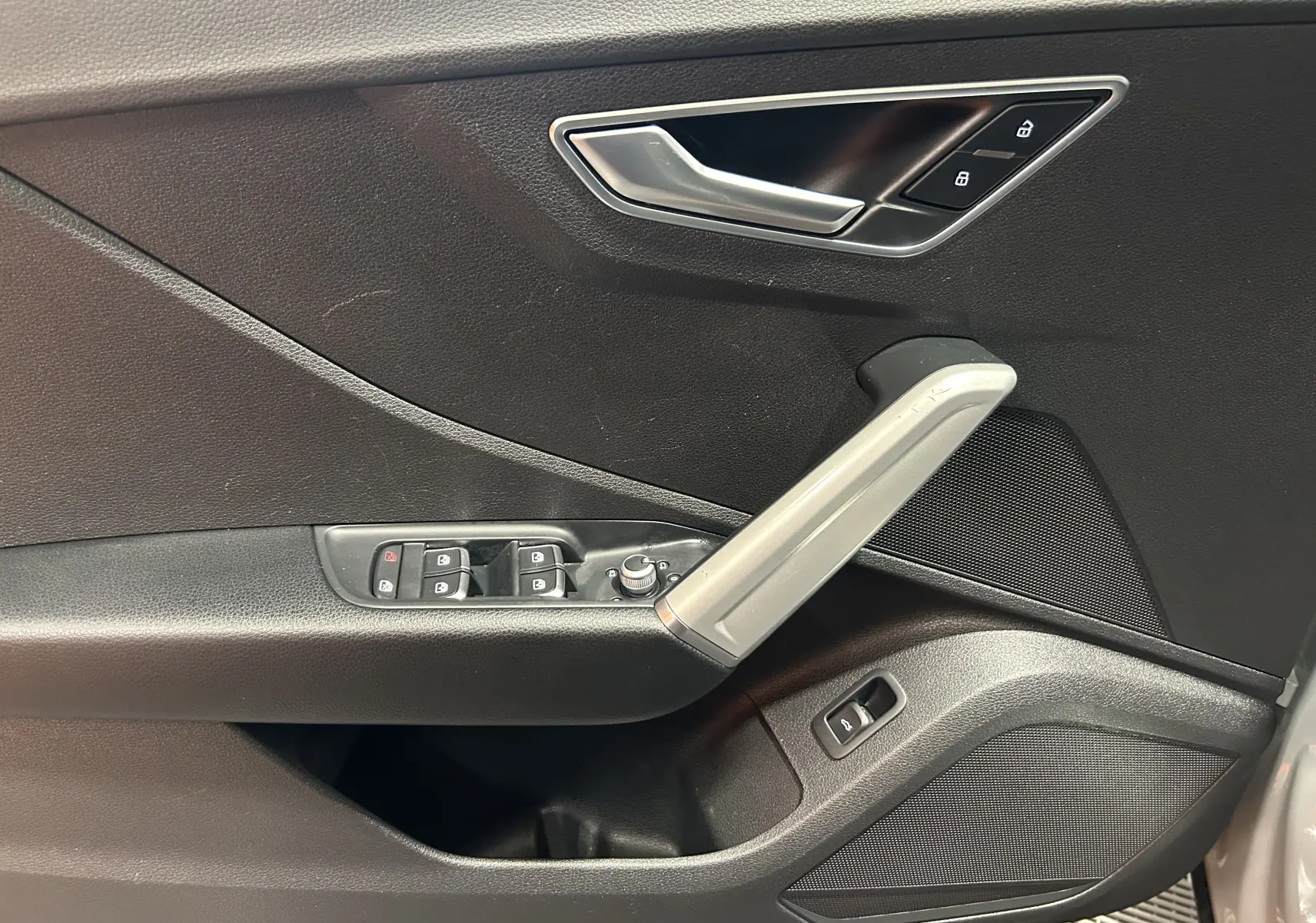 Vue rapprochée de la porte intérieure côté conducteur de l'Audi Q2 gris avec commandes de vitres et poignée argentée.