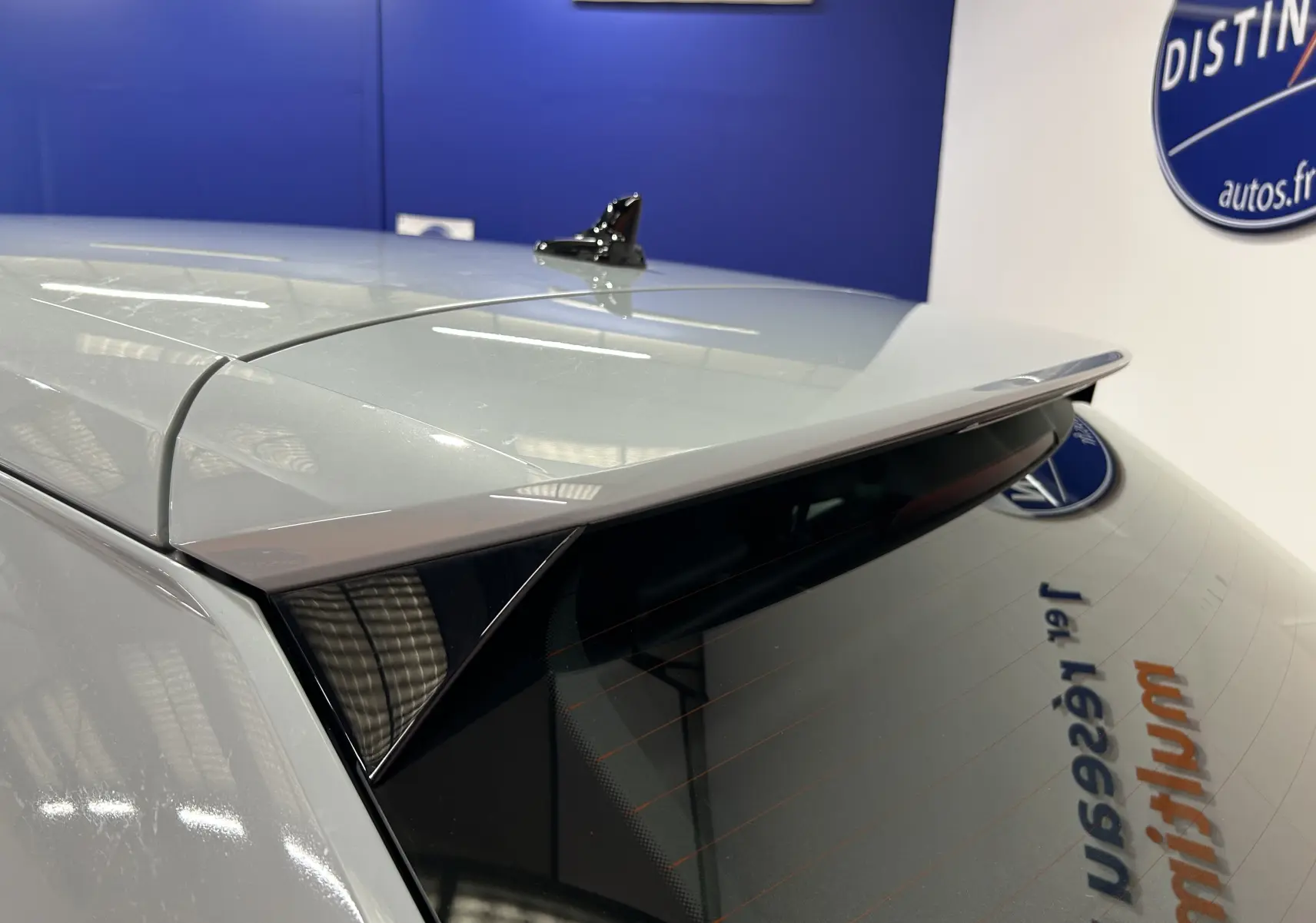 Détail du hayon arrière gris d’un Audi Q2 2023 avec antenne requin et vitre teintée en intérieur showroom.