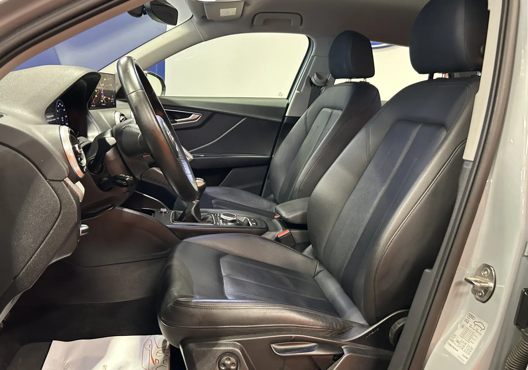 Vue intérieure côté conducteur de l'Audi Q2 gris, sièges cuir noirs et tableau de bord avec écran GPS visible.