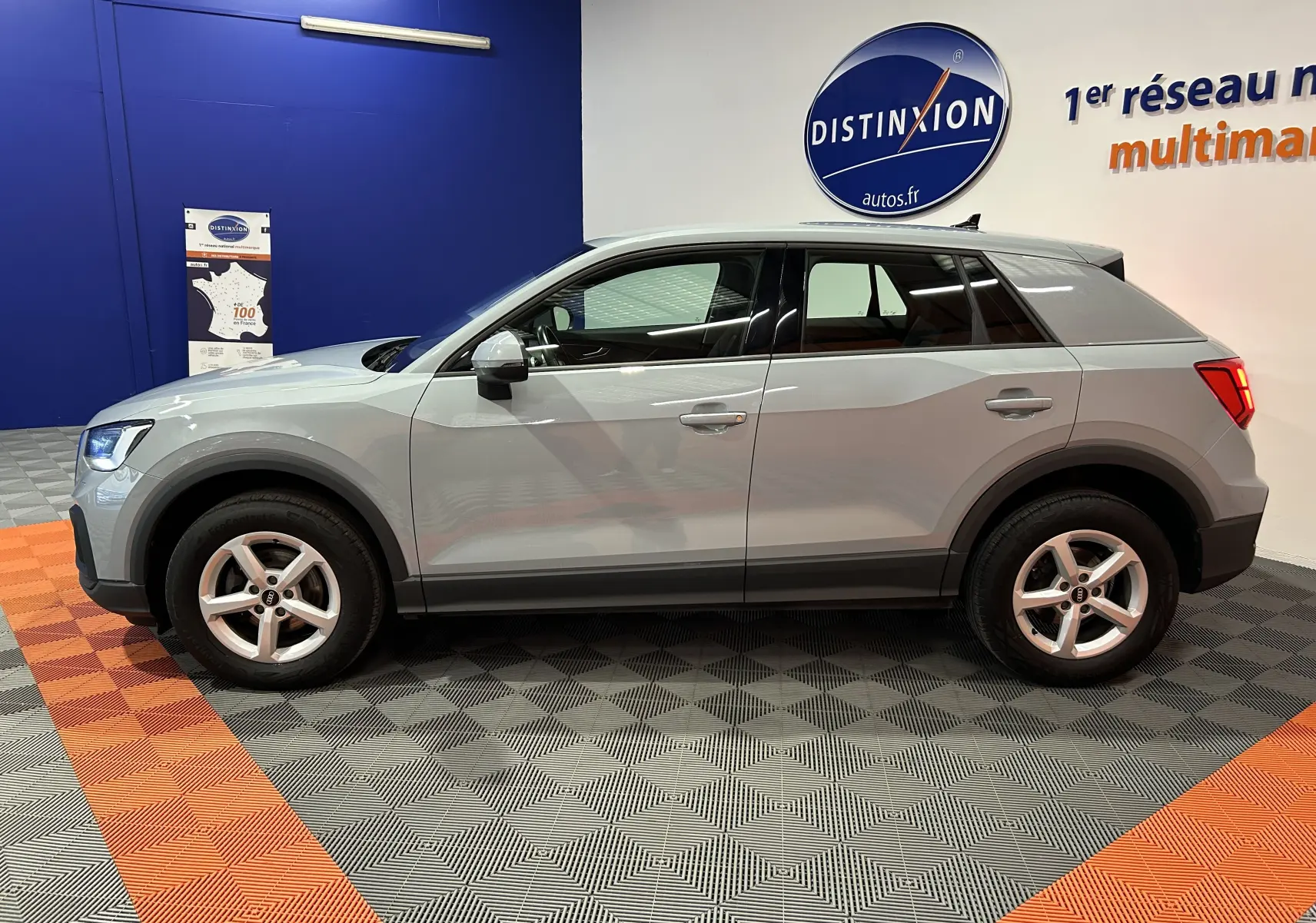 Audi Q2 gris vue de profil côté gauche dans un showroom avec jantes alliage et hayon électrique visible.
