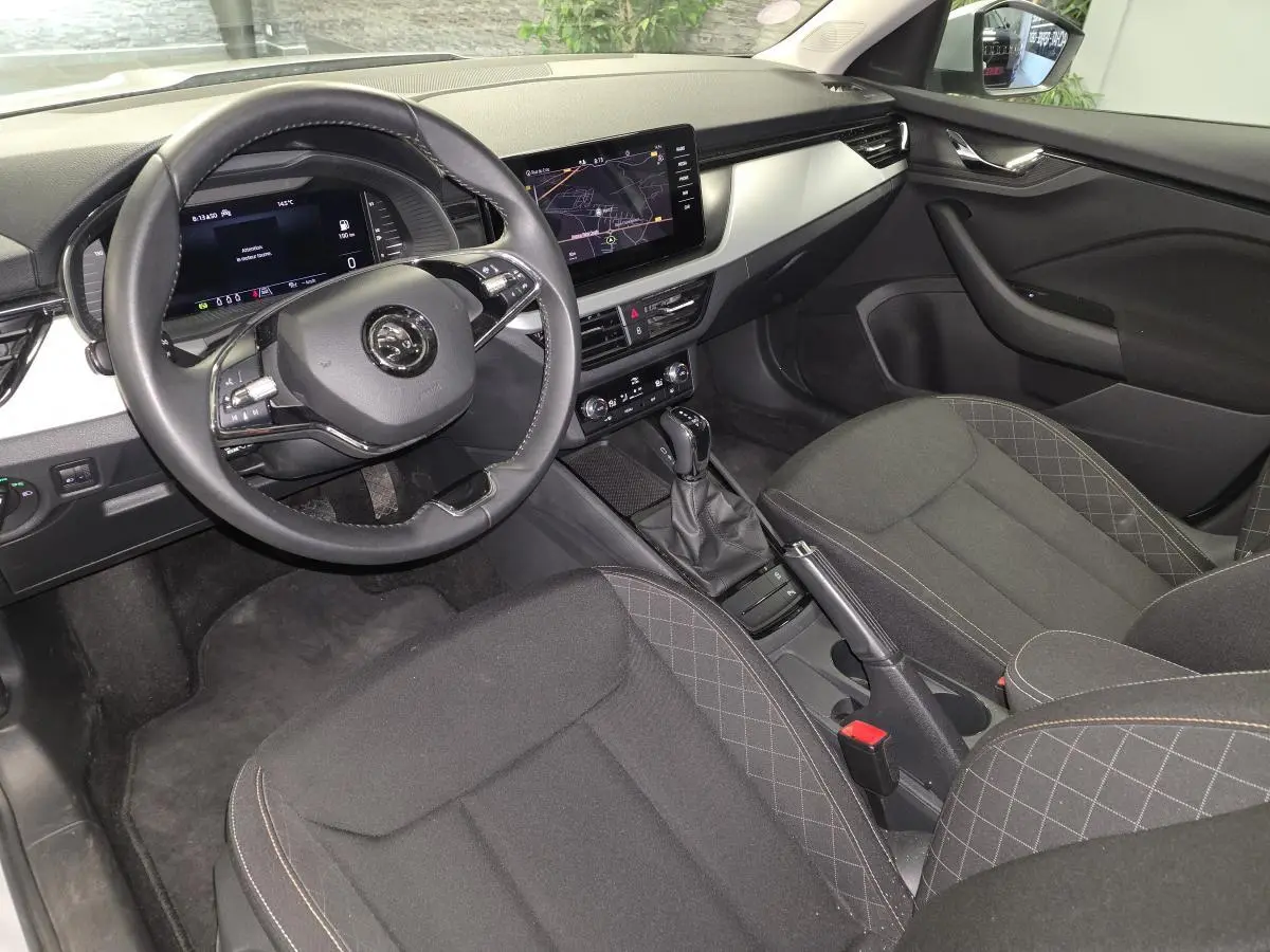 Vue intérieure côté conducteur du Skoda Kamiq 2023, avec volant cuir, écran tactile et sellerie tissu noire.