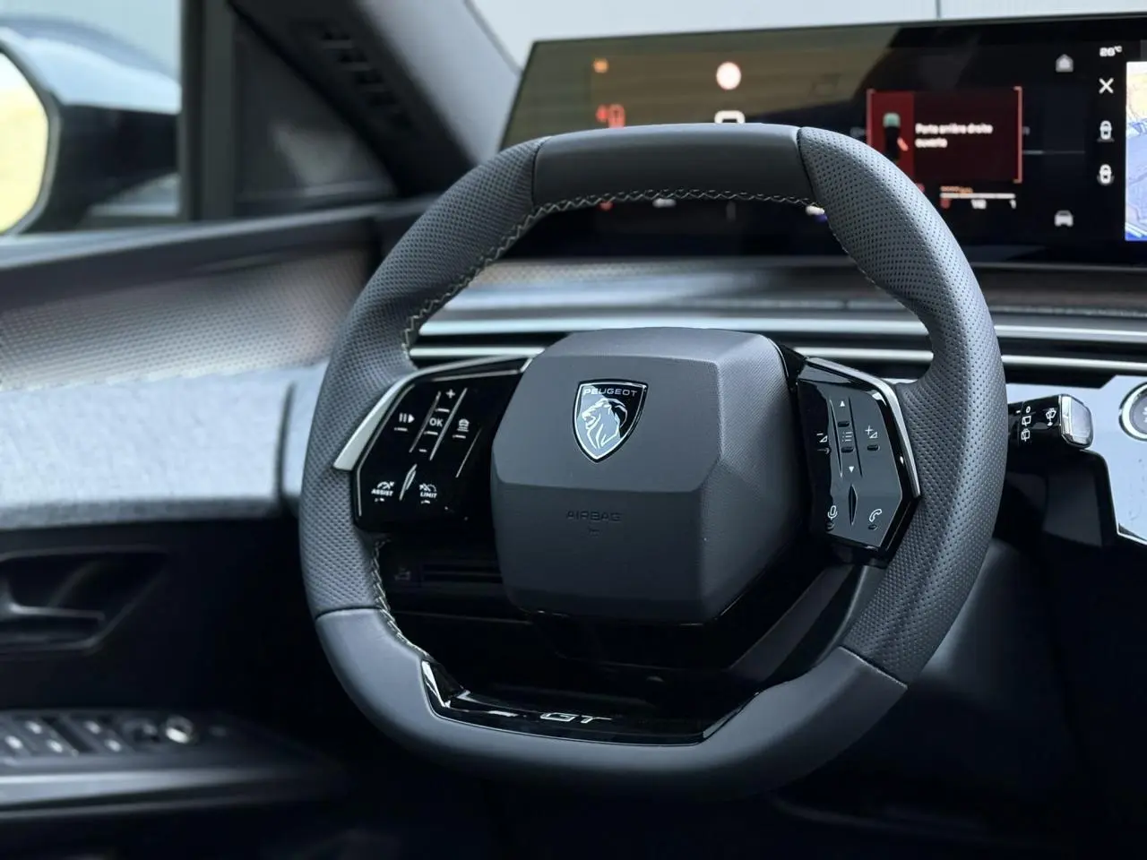 Volant compact Peugeot 5008 GT noir perforé avec commandes intégrées, vue rapprochée depuis le siège conducteur.
