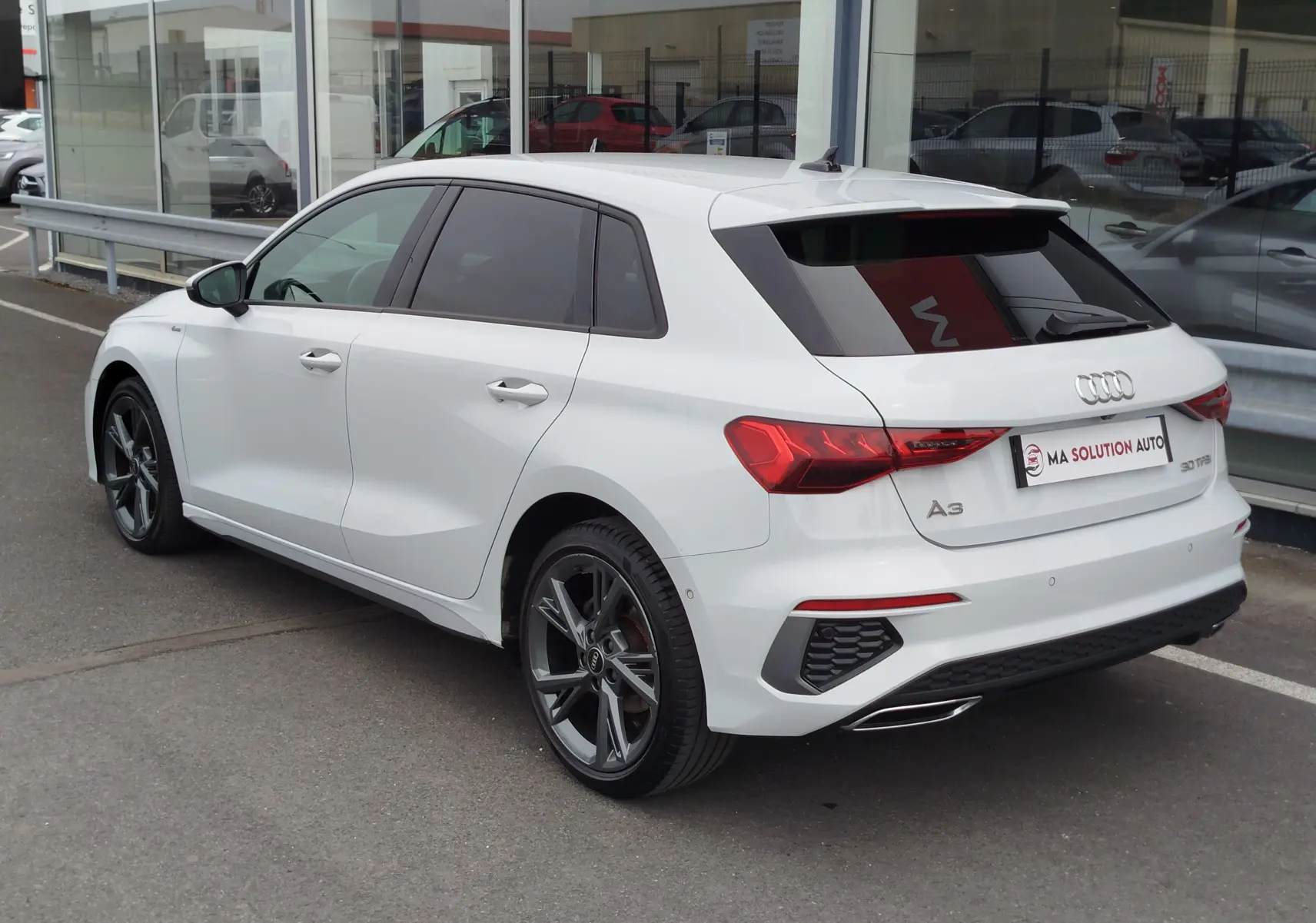 Audi A3 Sportback blanc Glacier métallisé vue 3/4 arrière droit avec jantes alliage et vitres teintées.