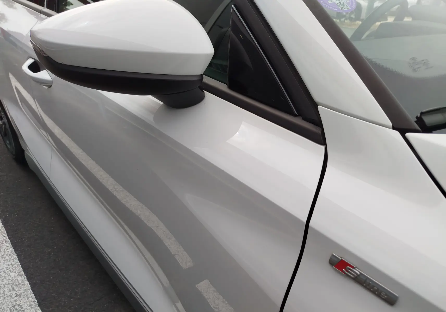 Vue rapprochée du côté gauche avant de l'Audi A3 Sportback blanc Glacier avec badge S line sur la portière.
