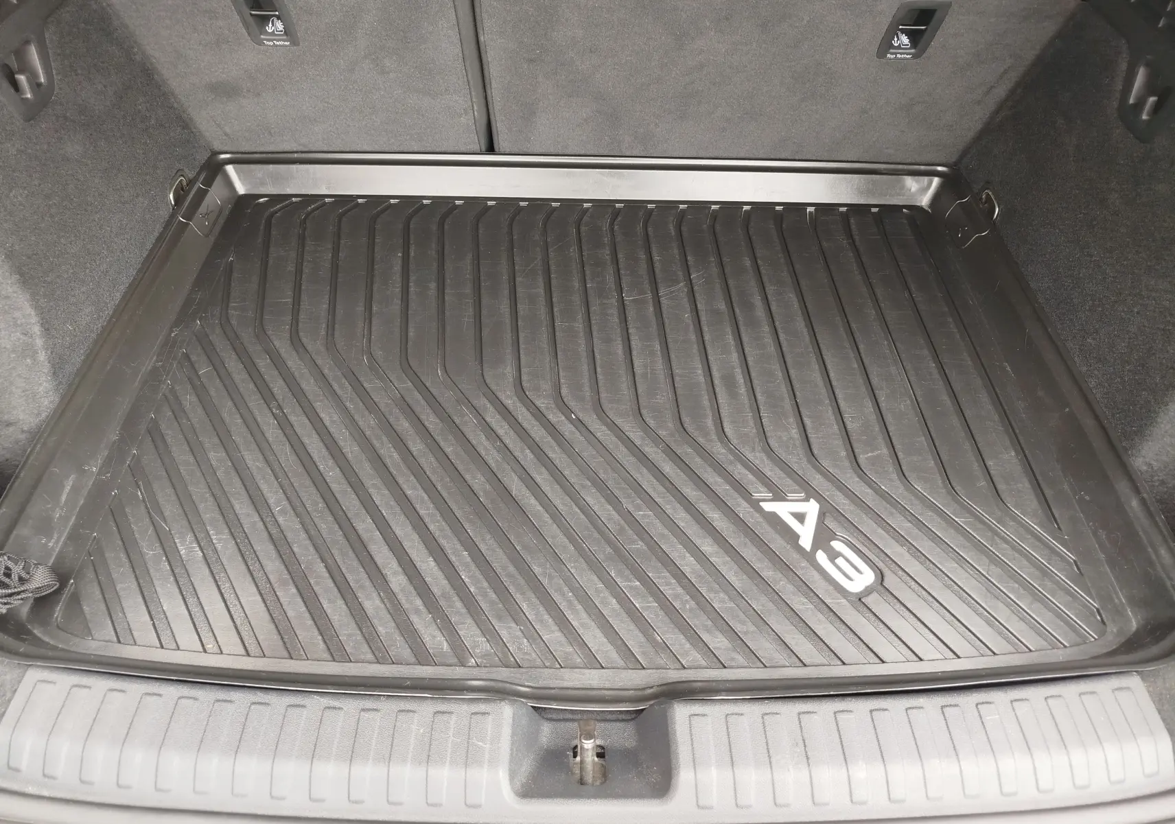 Vue plongeante sur le coffre avec tapis de protection noir marqué A3, intérieur gris foncé de l'Audi A3 Sportback.