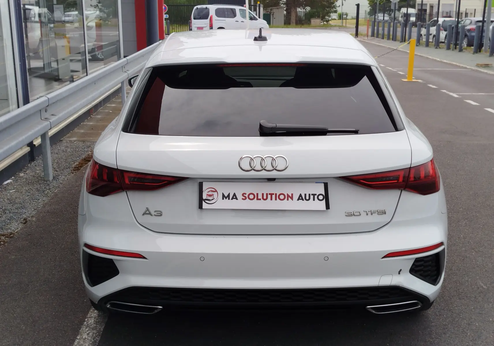 Vue arrière d'une Audi A3 Sportback blanc glacier métallisé avec feux LED et double sortie d'échappement intégrée.