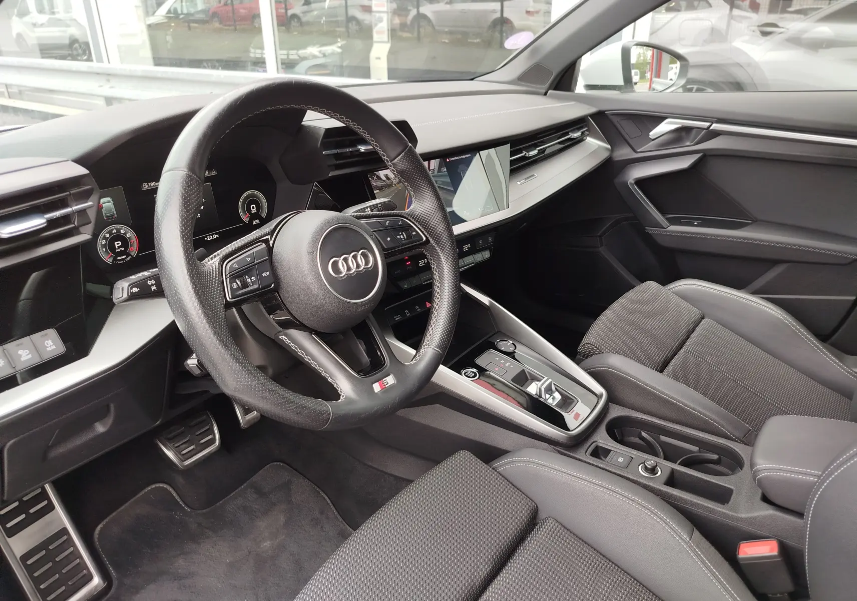 Vue intérieure côté conducteur de l'Audi A3 Sportback 30 TFSI S line 2022 avec volant sport et sellerie tissu gris.