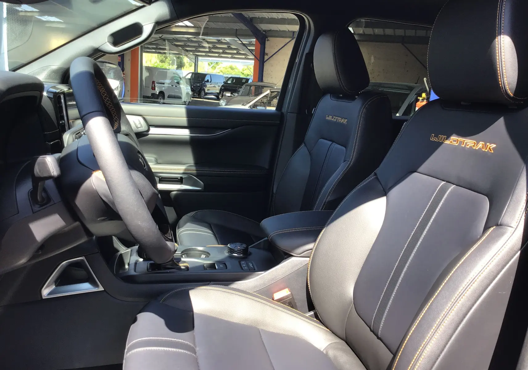 Vue intérieure côté conducteur du Ford Ranger Wildtrak 2025, sièges cuir noirs avec surpiqûres orange et logo brodé.