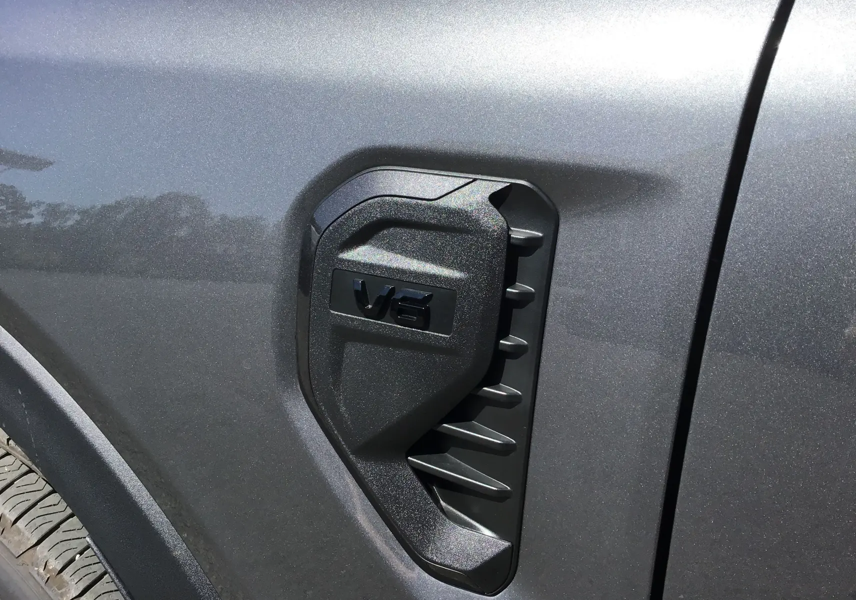 Détail de l'aération latérale noire avec logo V6 sur la portière côté gauche du Ford Ranger Wildtrak gris carbone 2025.