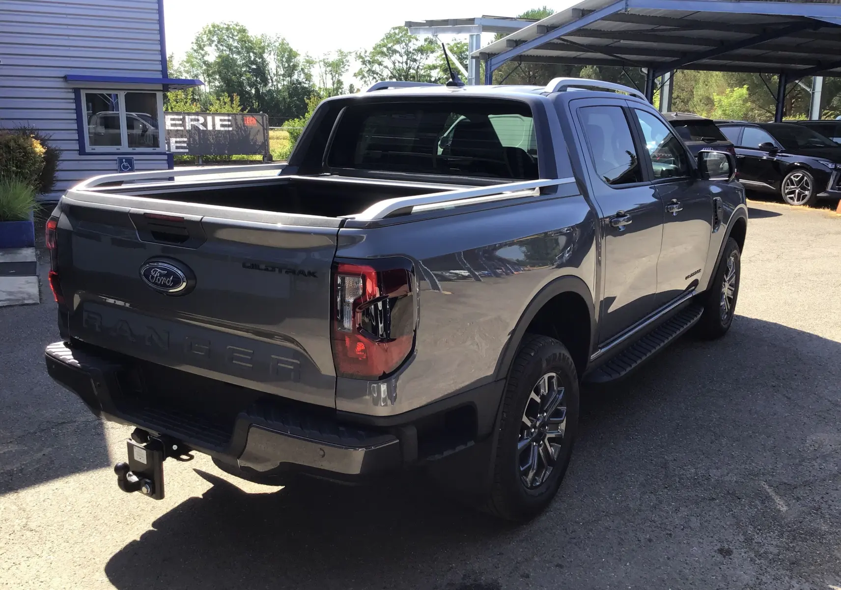 Ford Ranger Double Cabine gris carbone vu en 3/4 arrière droit, avec ridelle ouverte et attelage visible.