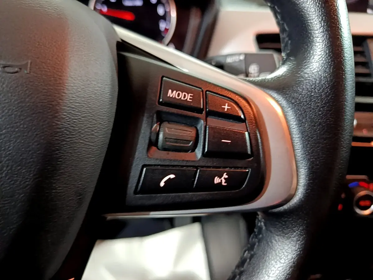 Gros plan sur le volant cuir et alu noir de la BMW X2 sDrive18i 2023, avec commandes multifonctions visibles.