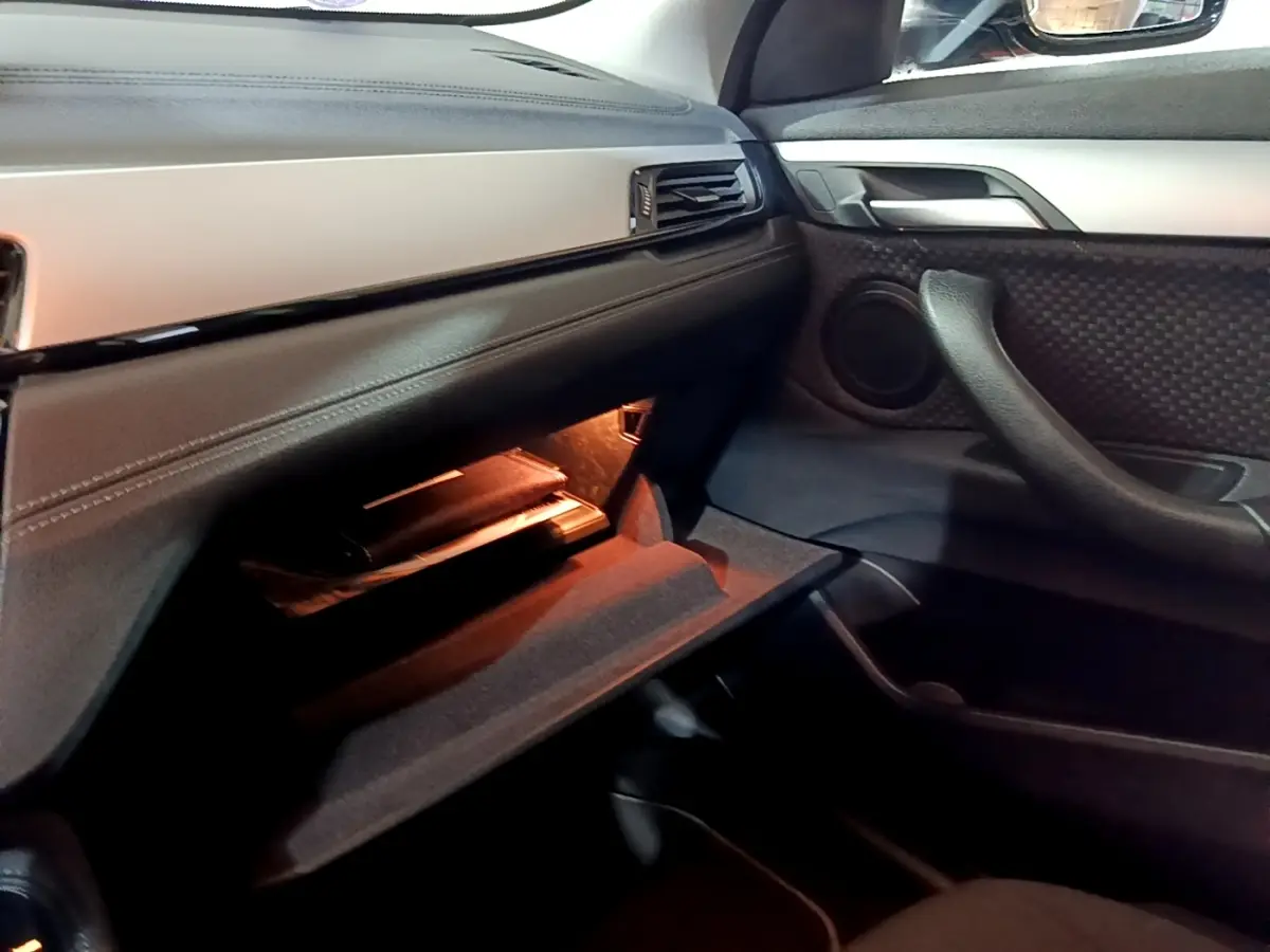 Intérieur BMW X2 sDrive18i Lounge 2023, vue côté passager sur boîte à gants ouverte avec éclairage ambiant noir.