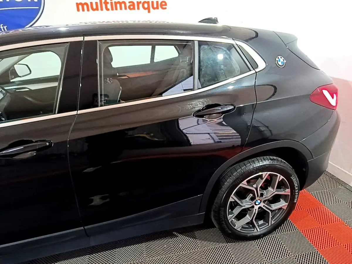 Vue latérale droite sur la partie arrière d’un BMW X2 noir 2023 avec jante alliage et logo BMW sur l’aile arrière.