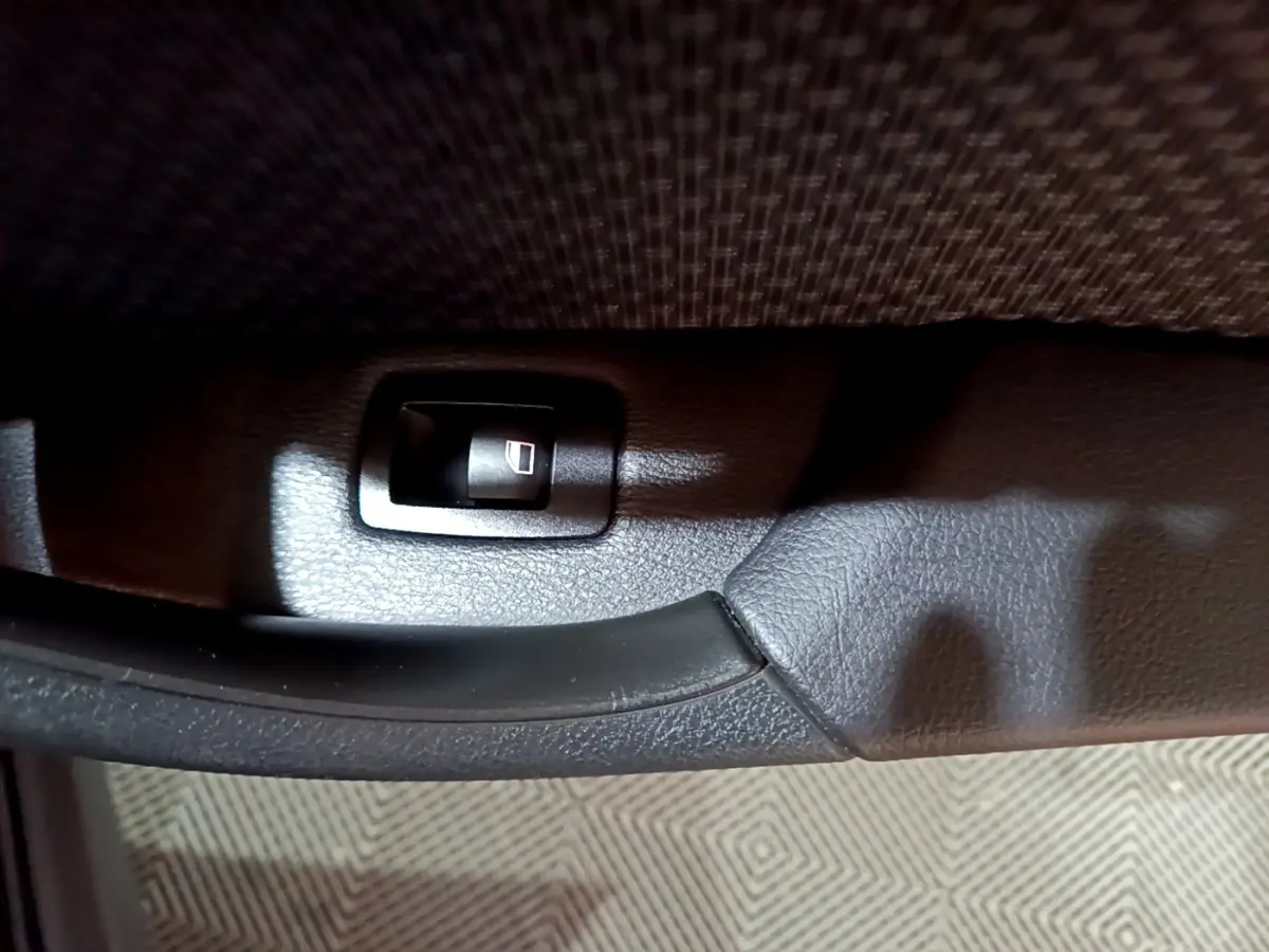 Gros plan sur la poignée intérieure noire et l’interrupteur de lève-vitre côté conducteur du BMW X2 noir 2023.