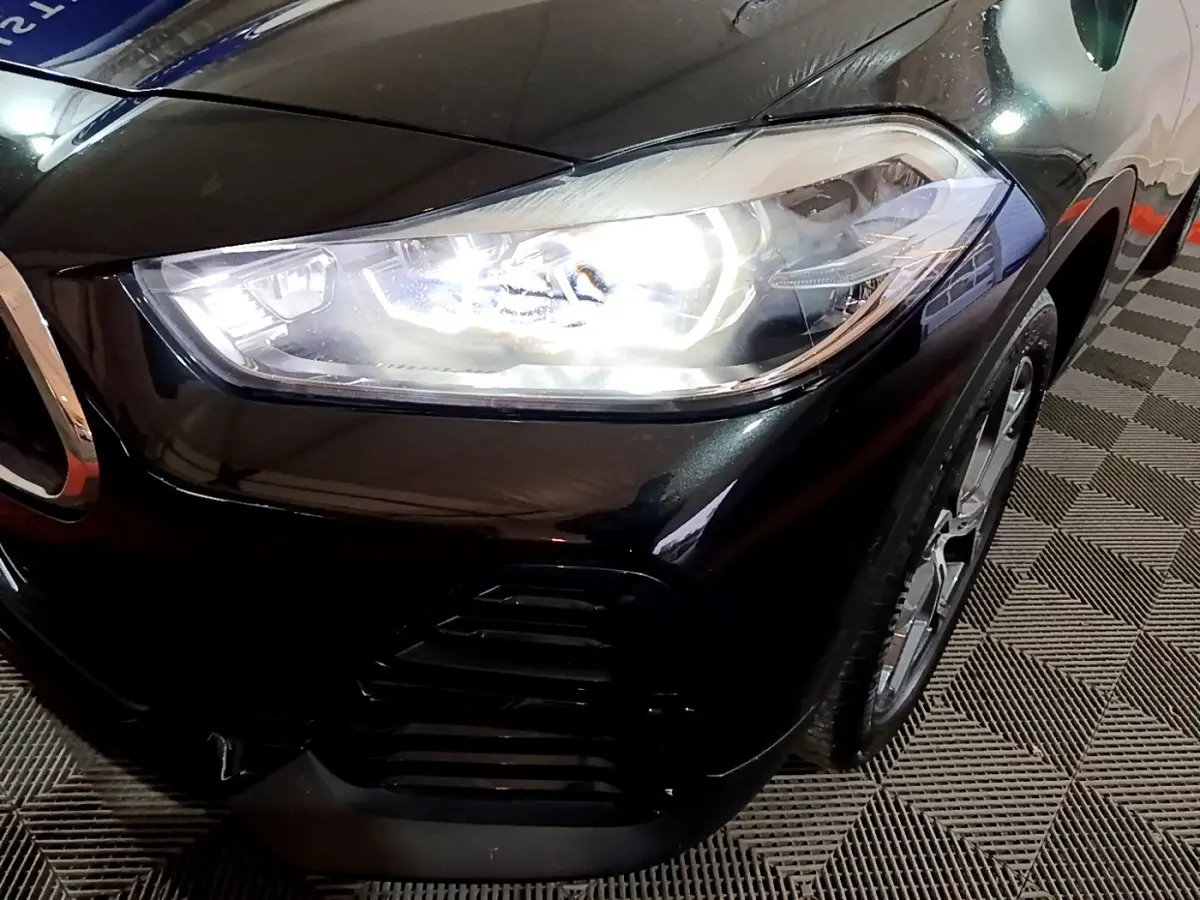 Gros plan sur l'avant droit noir brillant du BMW X2 sDrive18i 2023 avec phare LED allumé et jante visible.