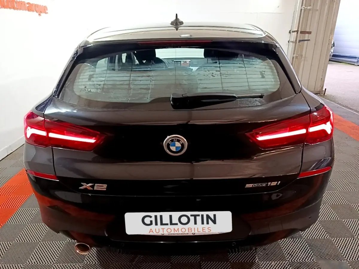 Vue arrière d’un BMW X2 sDrive18i noir avec feux LED allumés et logo visible sur fond intérieur showroom.