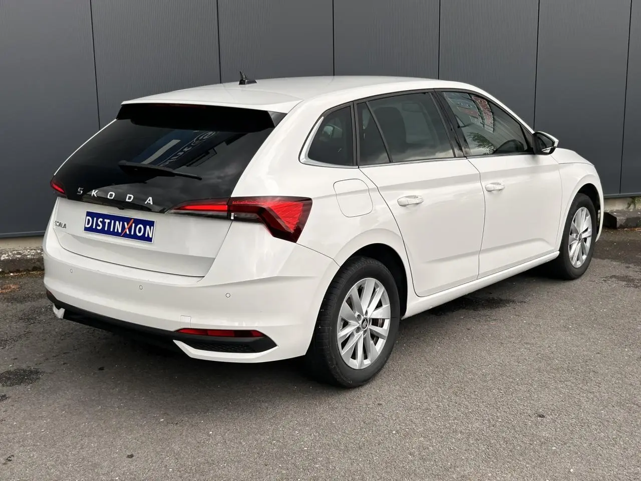 Vue 3/4 arrière droite d'une Skoda Scala blanc Candy avec lunette arrière surteintée et jantes alliage 16 pouces.