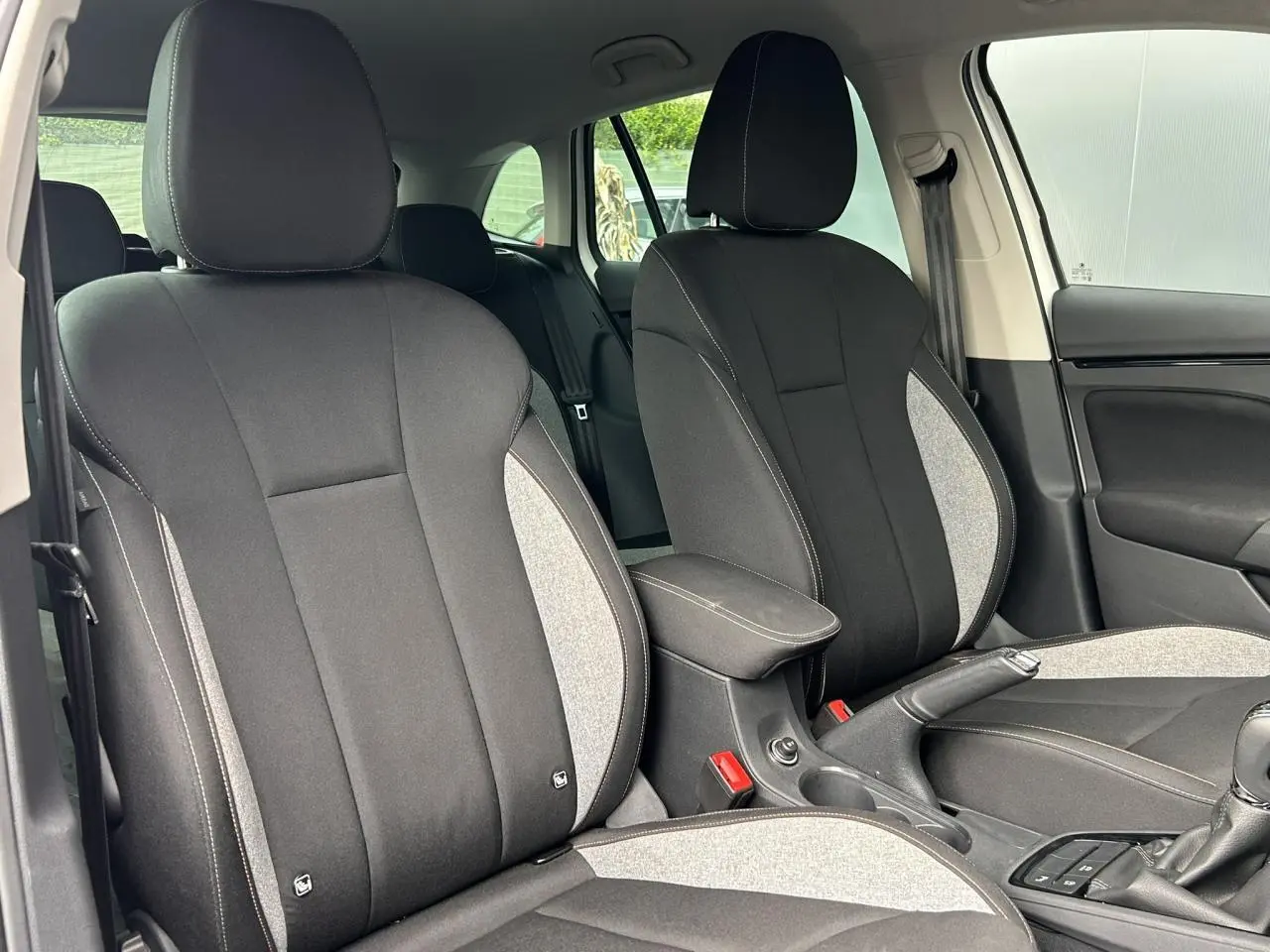Vue intérieure des sièges avant en tissu noir et gris de la Skoda Scala TSI 116 DSG7 Sélection, avec accoudoir central.