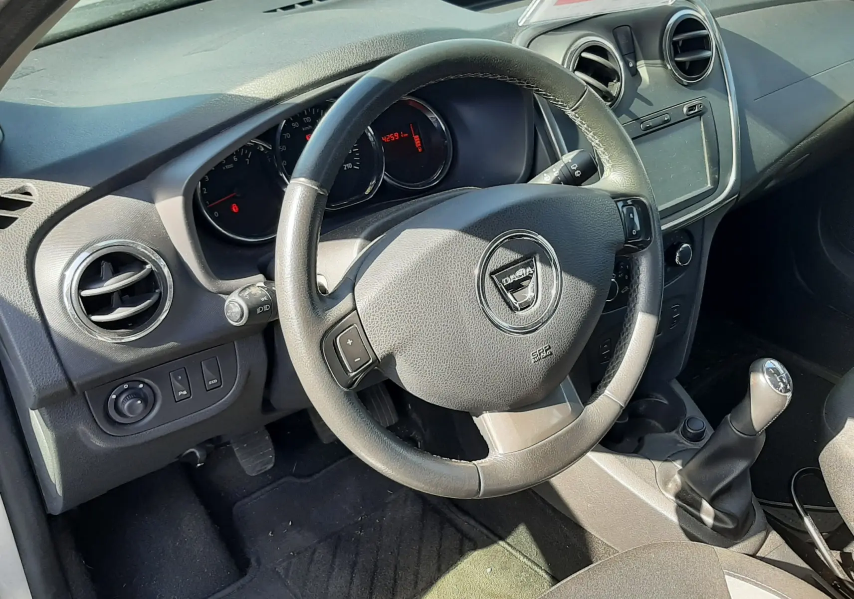 Vue intérieure côté conducteur de la Dacia Sandero Stepway 2016, volant multifonction et tableau de bord gris noir.