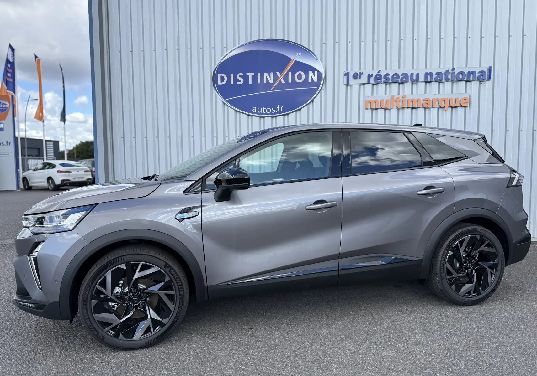Vue de profil droit du Renault Symbioz gris cassiopée métal, avec jantes noires au design dynamique, devant un mur avec logo Distinxion.