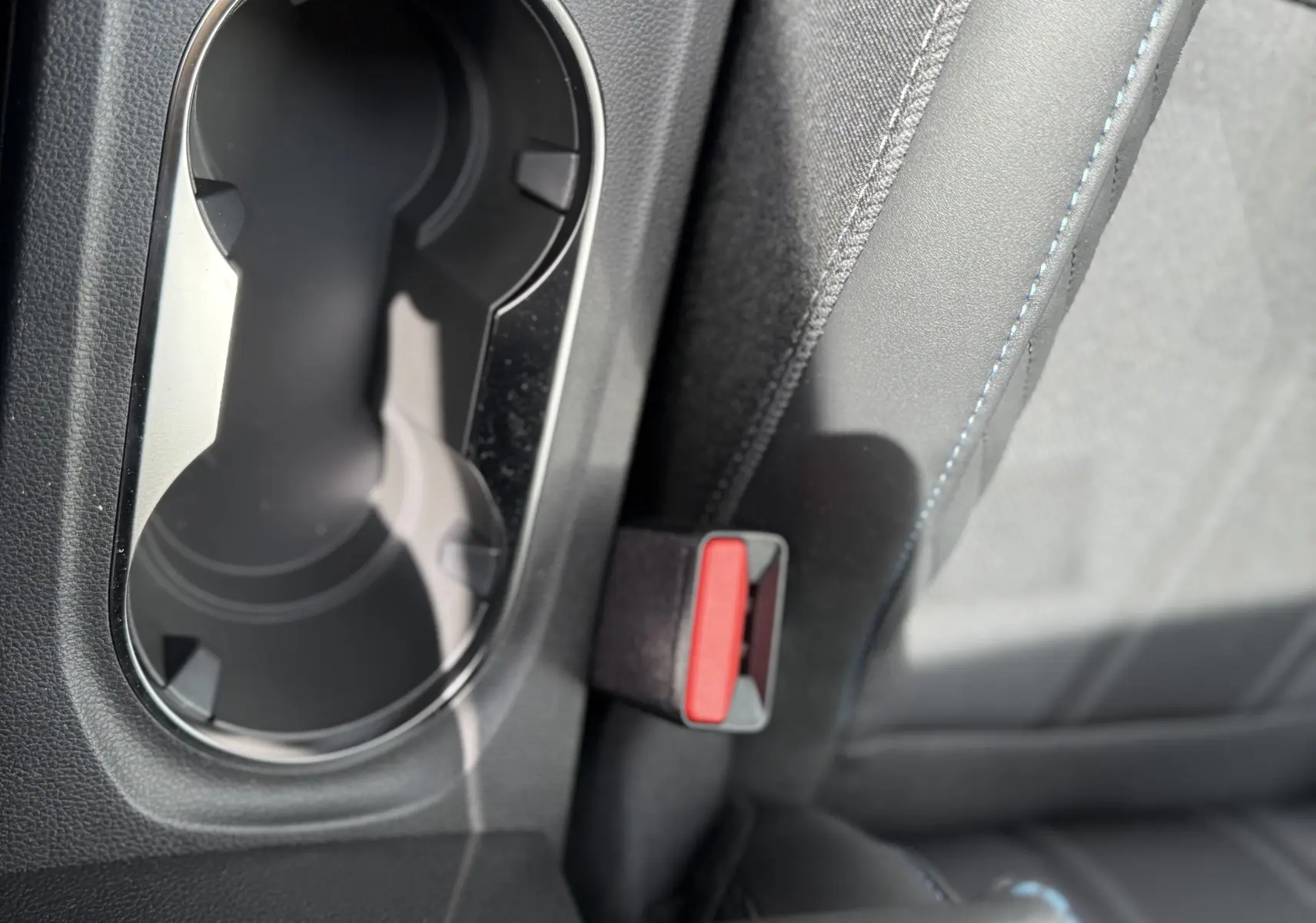 Gros plan sur la console centrale intérieure du Renault Symbioz gris cassiopée, avec porte-gobelets et bouton frein à main électrique.