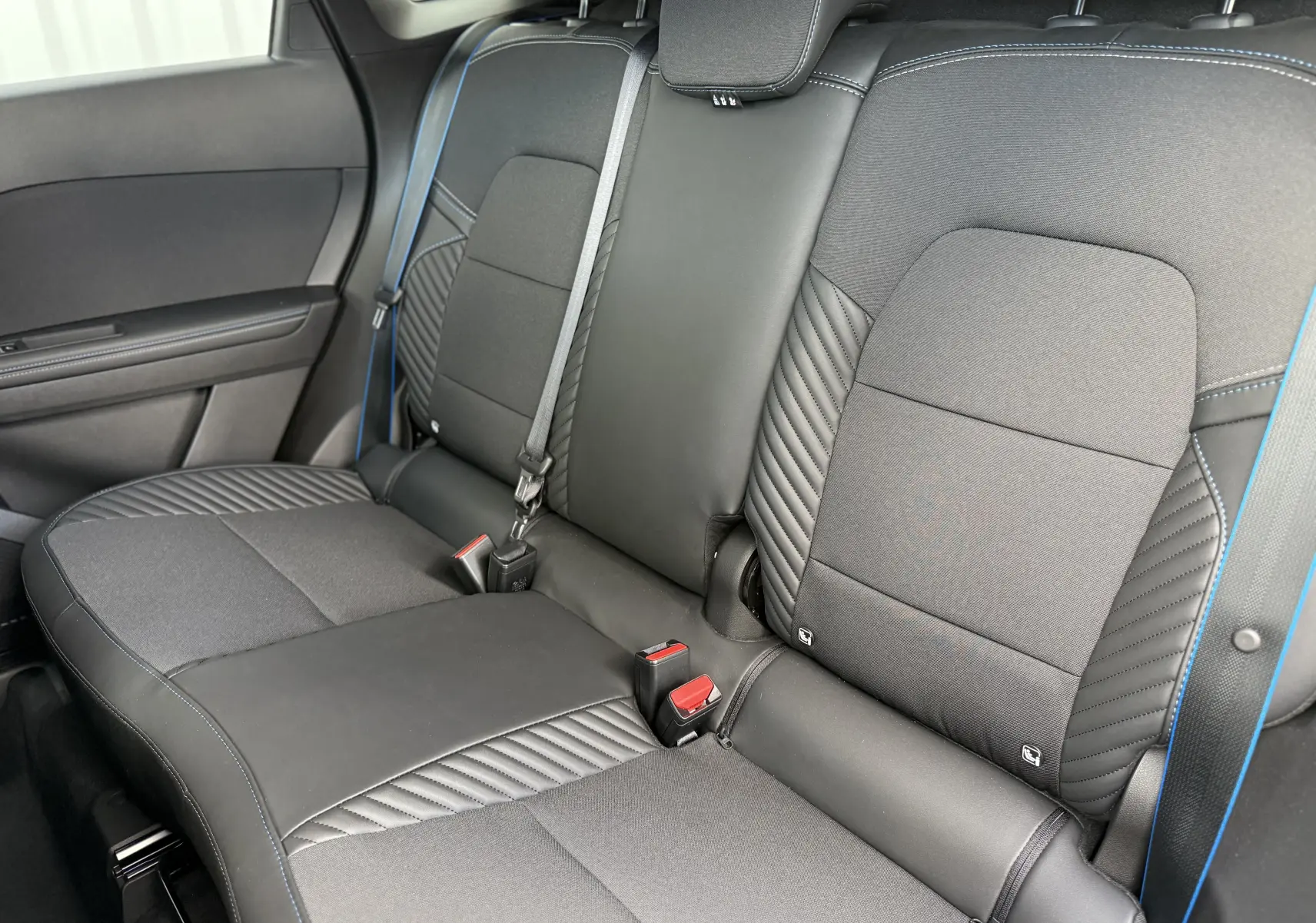 Vue intérieure arrière des sièges noirs et gris du Renault Symbioz Esprit Alpine, avec surpiqûres bleues et ceintures visibles.